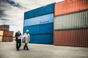 Maritime shipping manager and port worker at a commercial dock assessing freight logistics